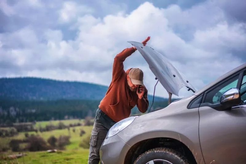 Man in rural area on phone looking under car bonnet