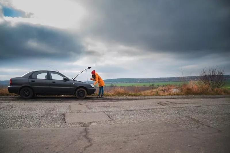Woman in rural area looking under car bonnet