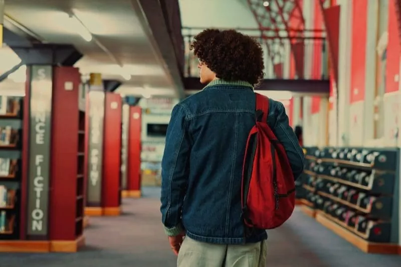 Person in library with backpack on shoulder