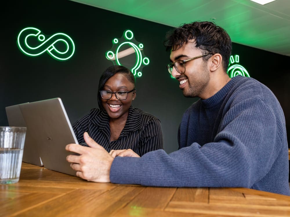 Man and woman smiling whilst working on laptops